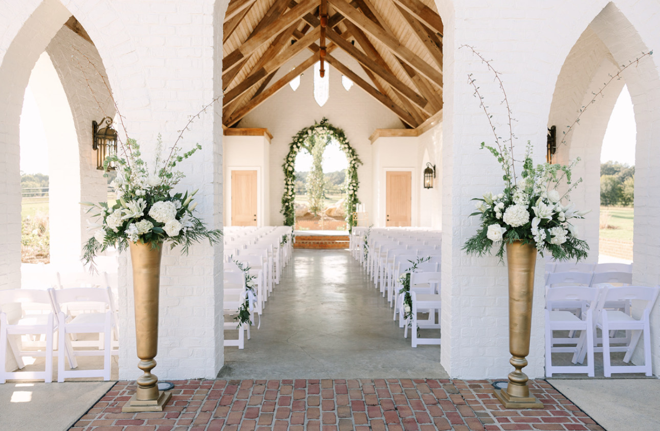 White floral arrangements in brass urns framing the chapel aisle beneath its arches